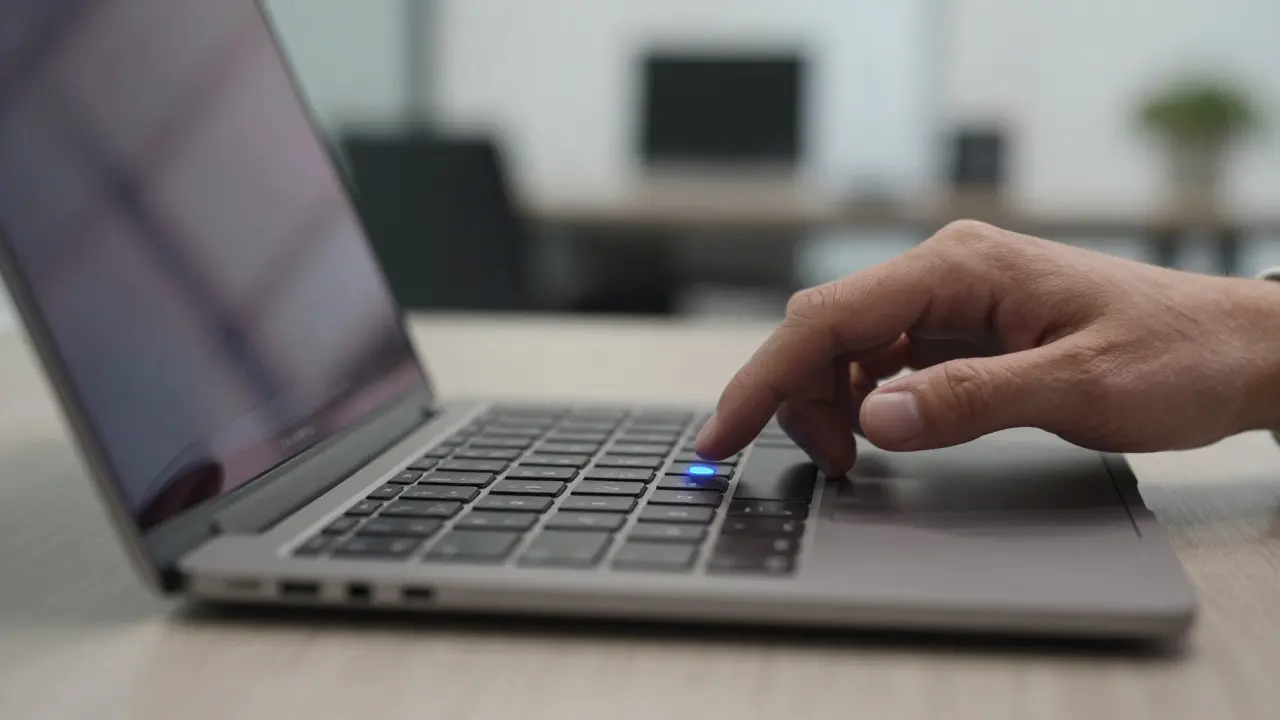 Thumb resting on the glowing Touch ID sensor of an Apple Magic Keyboard next to a laptop